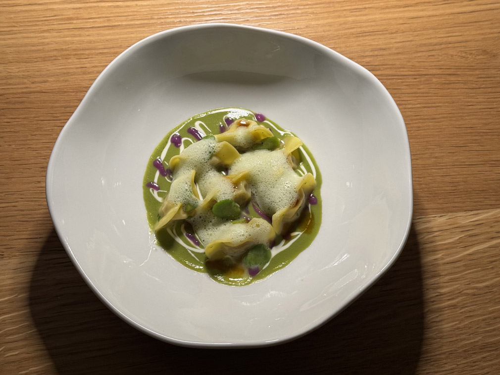 Cappellacci ripieni di cappone e anatra mantecati nel fondo di cottura, con crema di fave, stracciatella, cavolo cappuccio viola e aria di fave © Fermata Spettacolo